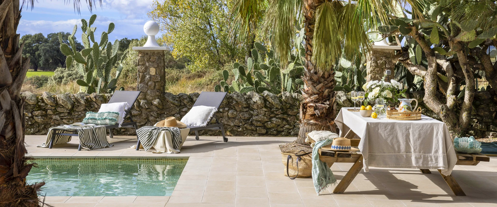 Casa con piscina privada en Toledo con tumbonas junto a un muro de piedra y mesa de comida bajo las palmeras