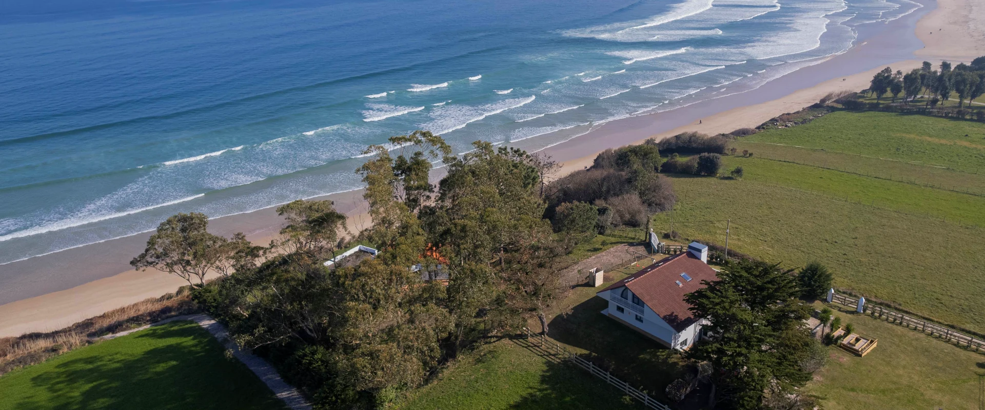 Villas de lujo en la playa con vistas al mar, casa entre árboles y prados frente a una playa de arena con olas